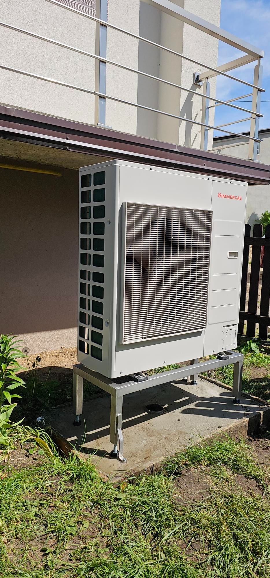 Zewnętrzna jednostka hybrydowej pompy ciepła Immergas Magis Combo Plus 9 V2 umieszczona na metalowym stelażu z regulowanymi nóżkami, na betonowej wylewce, z widocznym logo producenta.