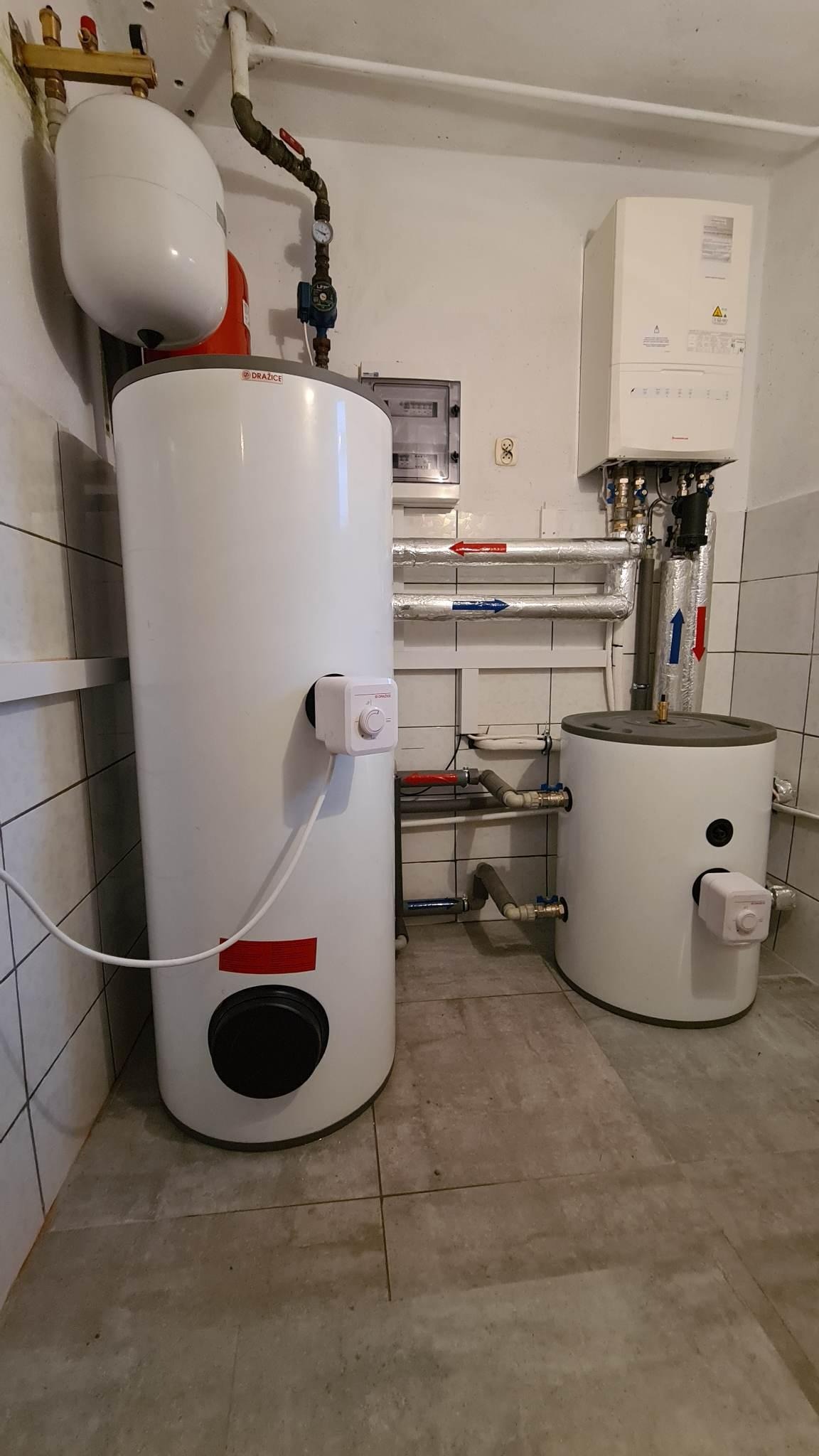 Dwa białe zasobniki ciepłej wody użytkowej (CWU) marki Drazice i A.J., z widocznymi przewodami instalacji CO i CWU, zamontowane w pomieszczeniu z wykończeniem w płytkach ceramicznych.