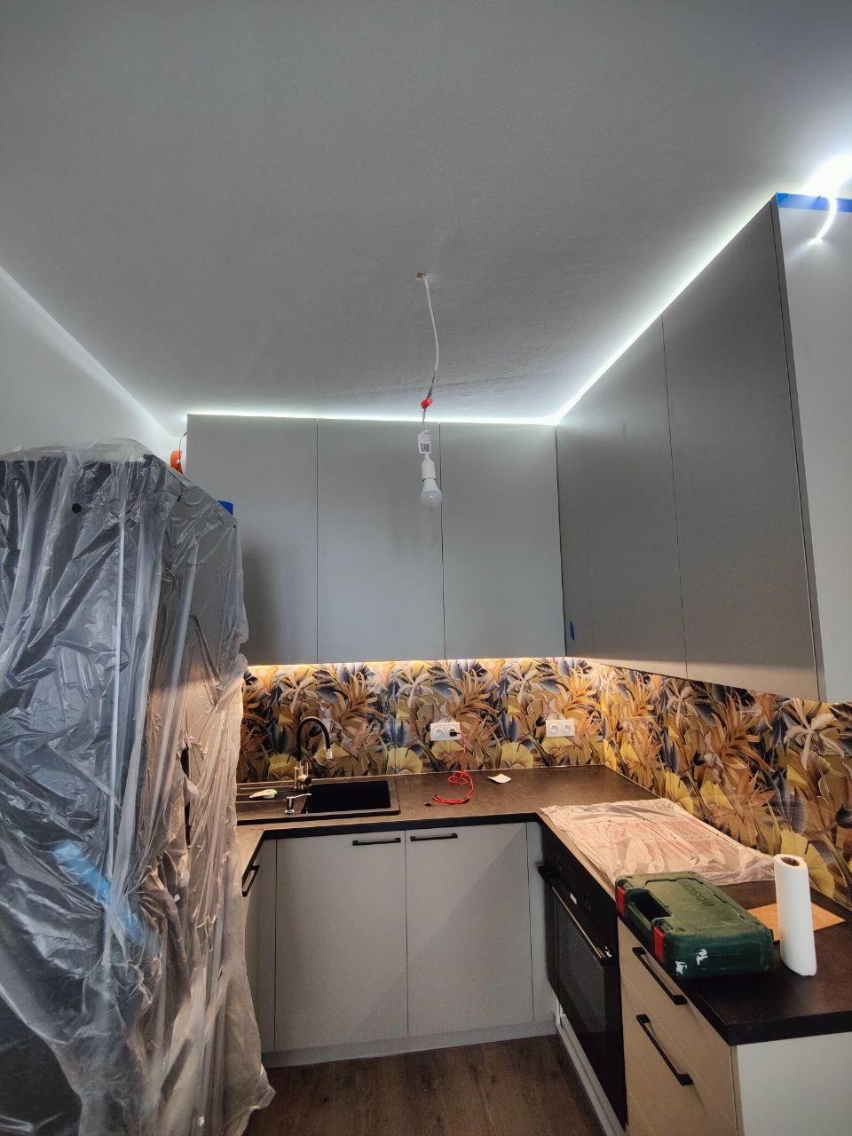 Kuchnia po remoncie: zabudowa meblowa z podświetleniem LED, dekoracyjna ściana nad blatem. Lodówka zabezpieczona folią. Widoczne narzędzia i akcesoria.