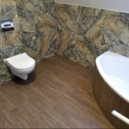 Nowoczesna łazienka z brązowymi płytkami imitującymi drewno na podłodze i ścianach, z elementami dekoracyjnymi przypominającymi kamień, wisząca toaleta i wanna.