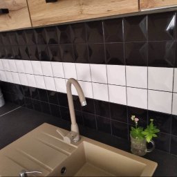 Sonbud - Czarno-biała glazura ścienna w kuchni z beżowym zlewem i minimalistyczną baterią, uzupełniona małą rośliną w szklance z uchem.