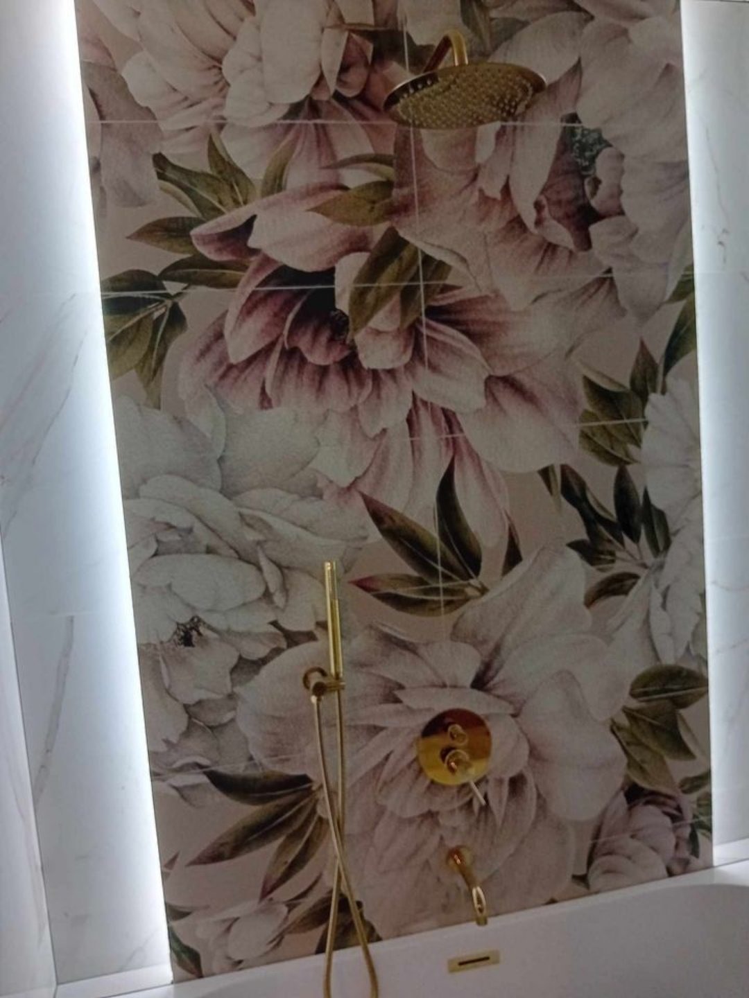 Łazienka z dekoracyjnymi płytkami w kwiaty i złotą armaturą, oświetlenie LED po bokach