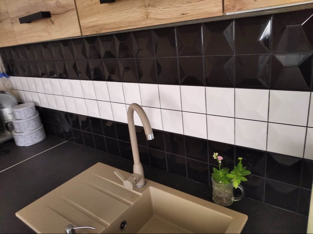 Czarno-biała glazura ścienna w kuchni z beżowym zlewem i minimalistyczną baterią, uzupełniona małą rośliną w szklance z uchem.