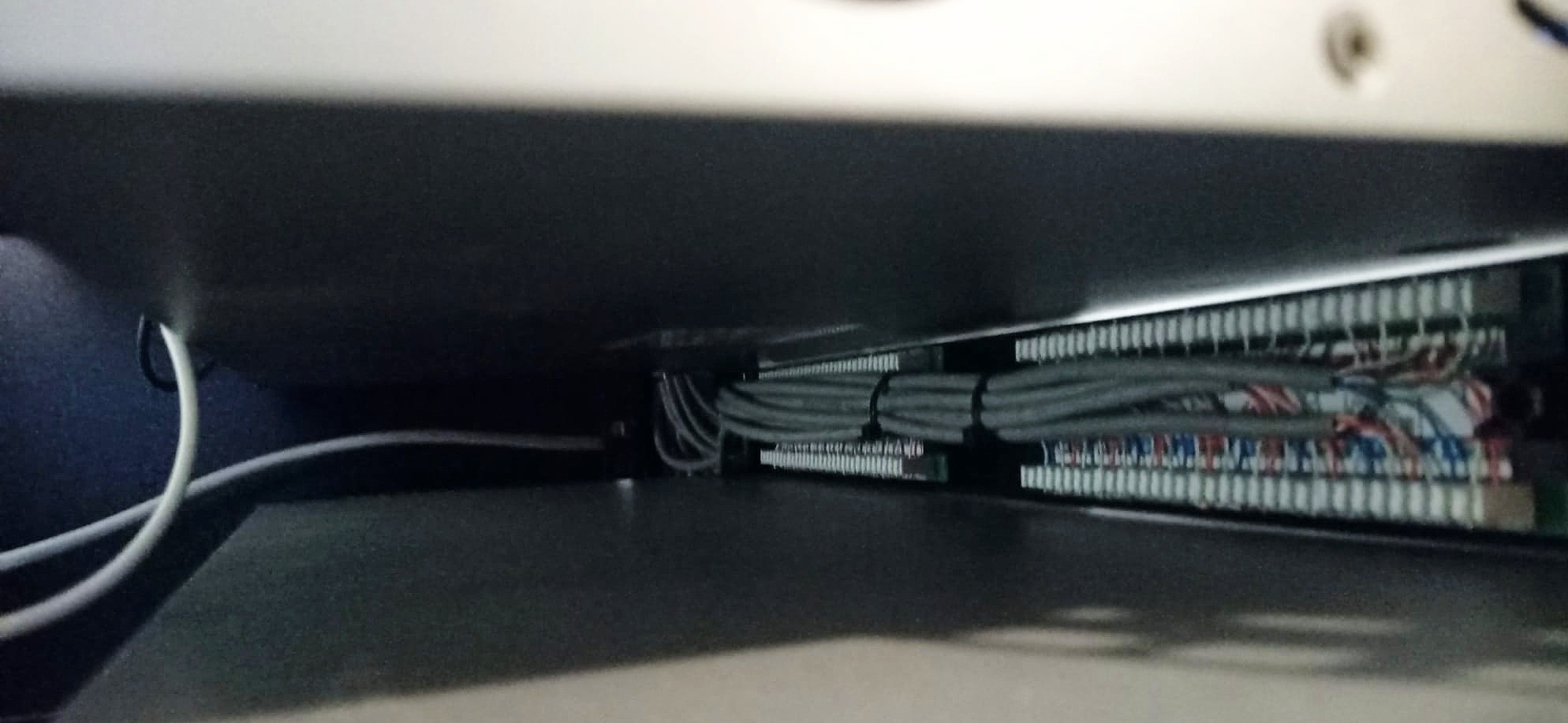 Widok z dołu na kable sieciowe uporządkowane w szafie serwerowej, z widocznymi złączami i panelami krosowniczymi.