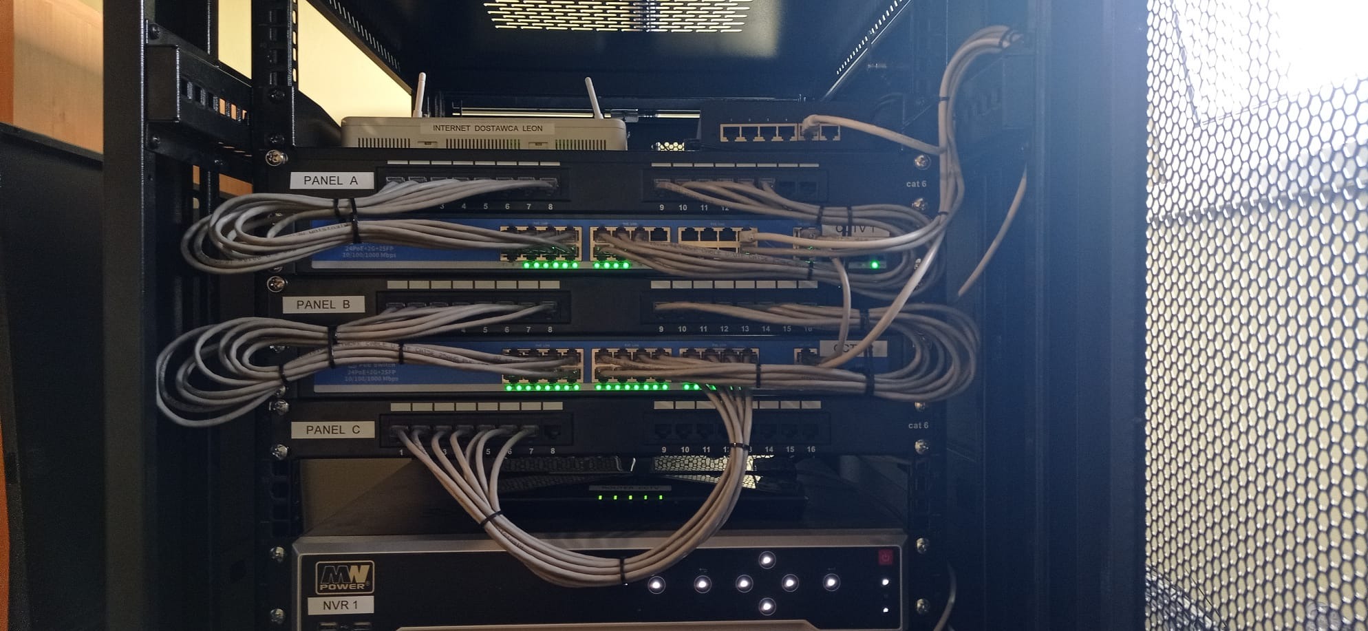 Ruter i przełączniki sieciowe zamontowane w szafie rack, z widocznymi kablami sieciowymi i diodami LED sygnalizującymi aktywność portów.