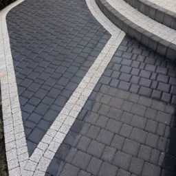 Ułożona kostka brukowa w odcieniach szarości z białymi obrzeżami i schodami, widok z góry pod kątem.