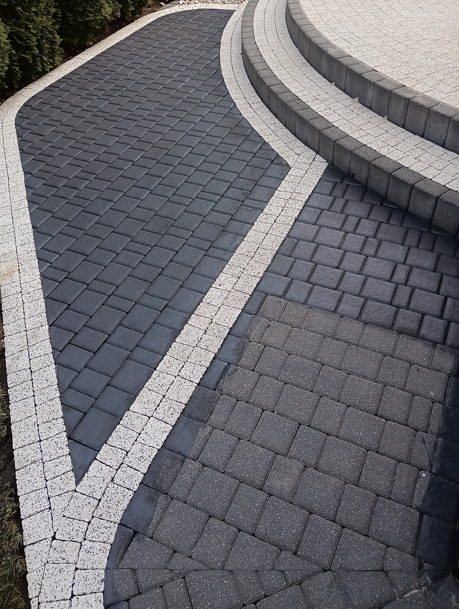 Ułożona kostka brukowa w odcieniach szarości z białymi obrzeżami i schodami, widok z góry pod kątem.