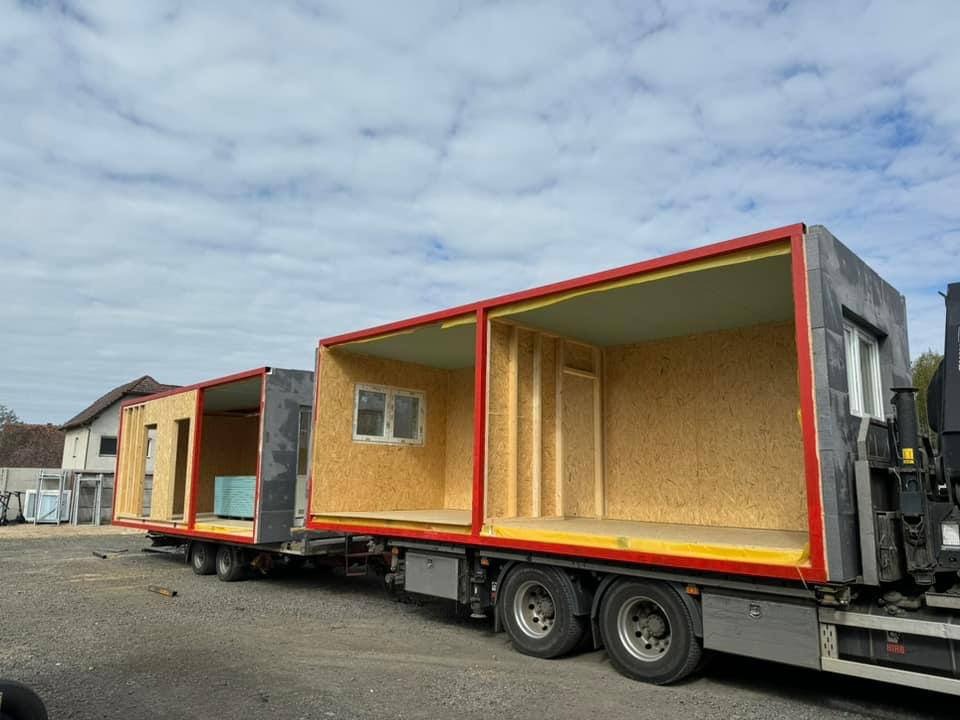 Transport dwóch modułów domu prefabrykowanego na naczepie, widoczne okno w jednym z modułów, konstrukcja szkieletowa i płyty OSB, pochmurne niebo w tle.