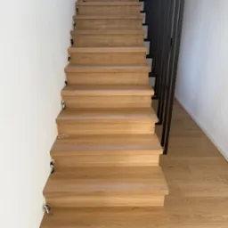 Naturalne, jasne schody z drewna dębowego z czarną, minimalistyczną balustradą. Widok z dołu, podkreślający fakturę drewna i nowoczesny design.