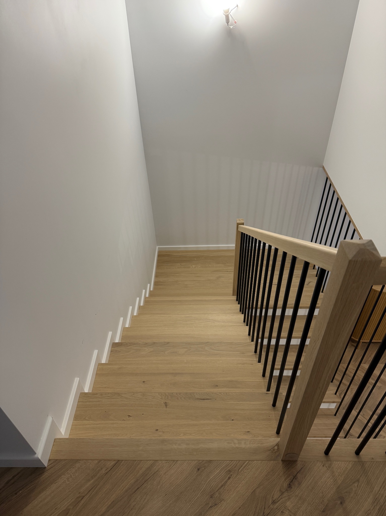 Jasne, dębowe schody z czarną balustradą w Sandomierzu, widziane z góry. Minimalistyczny design, białe ściany i listwy przypodłogowe. Nowoczesne wykończenie.