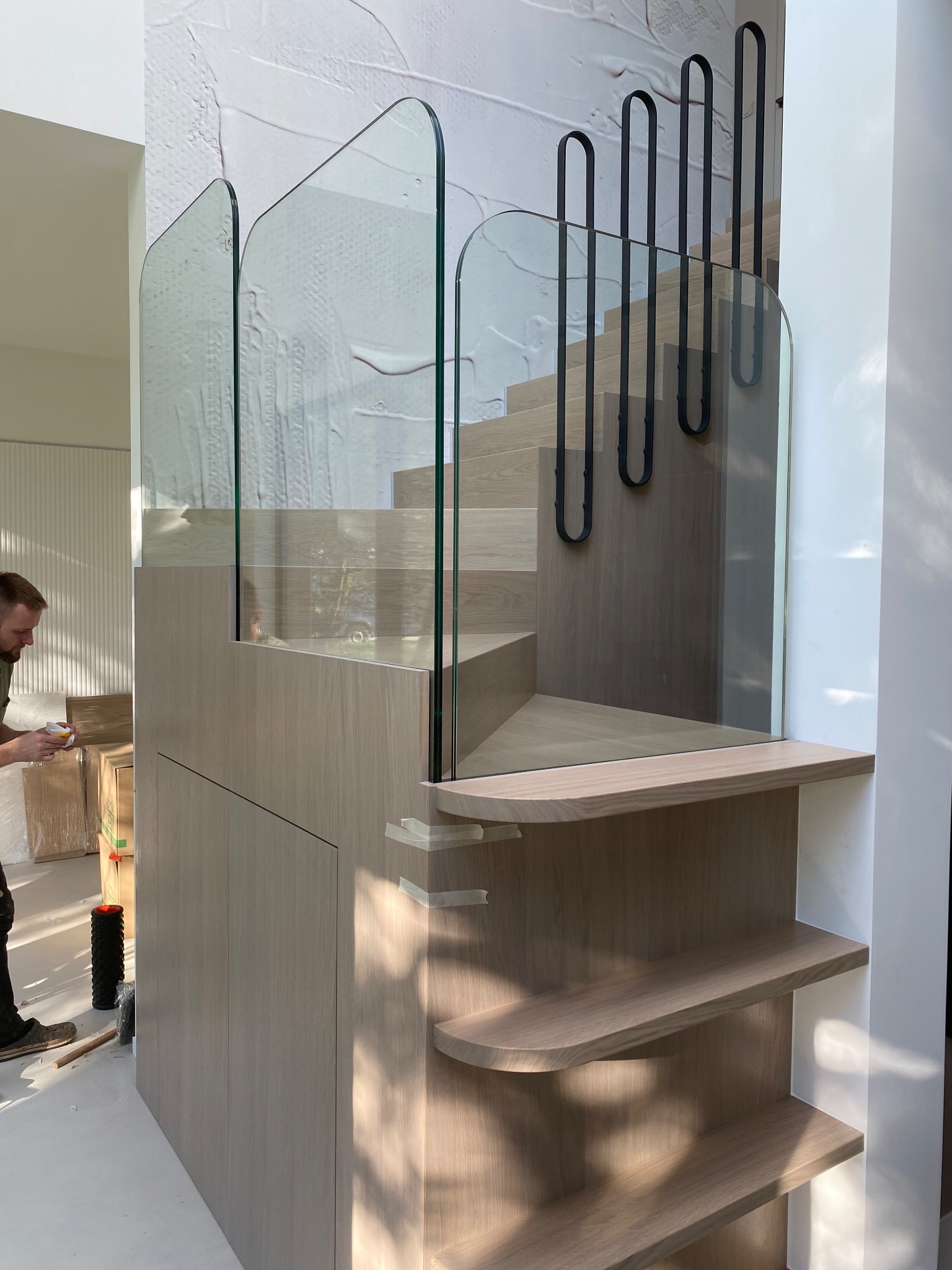 Nowoczesne schody z jasnego drewna i szklaną balustradą z czarnymi, metalowymi elementami w Bęczarce. Widoczne etapy montażu.