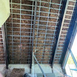 FHU Jakubiak - Skośny sufit poddasza w trakcie ocieplania wełną mineralną, widoczna metalowa konstrukcja nośna i przewody elektryczne.