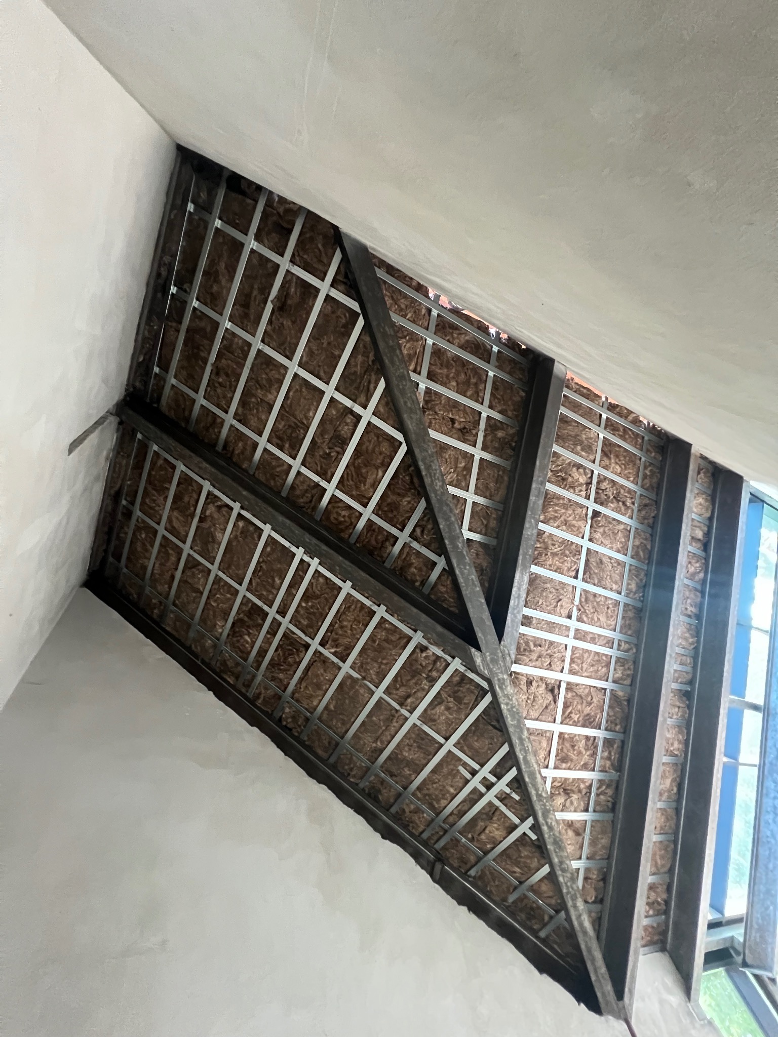 Poddasze w trakcie ocieplania: widoczna wełna mineralna i metalowa konstrukcja stelaża, surowy stan ścian, okno dachowe w tle.