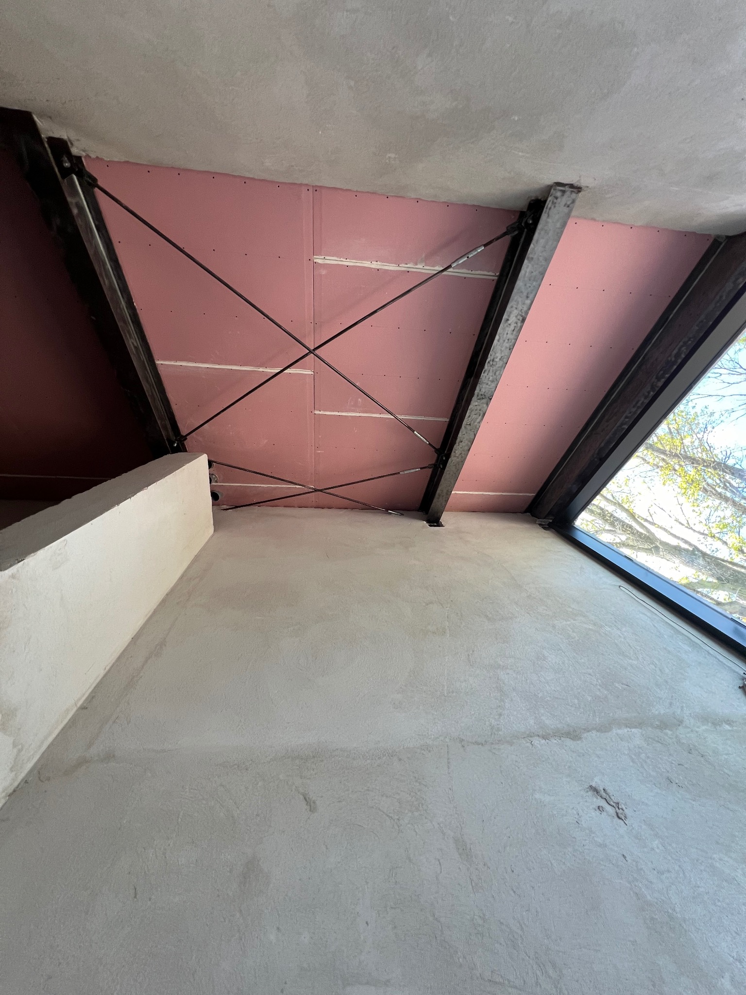 Poddasze w trakcie prac: surowe ściany, odsłonięta konstrukcja stalowa, płyty gipsowo-kartonowe na skośnym suficie, widok z dołu.