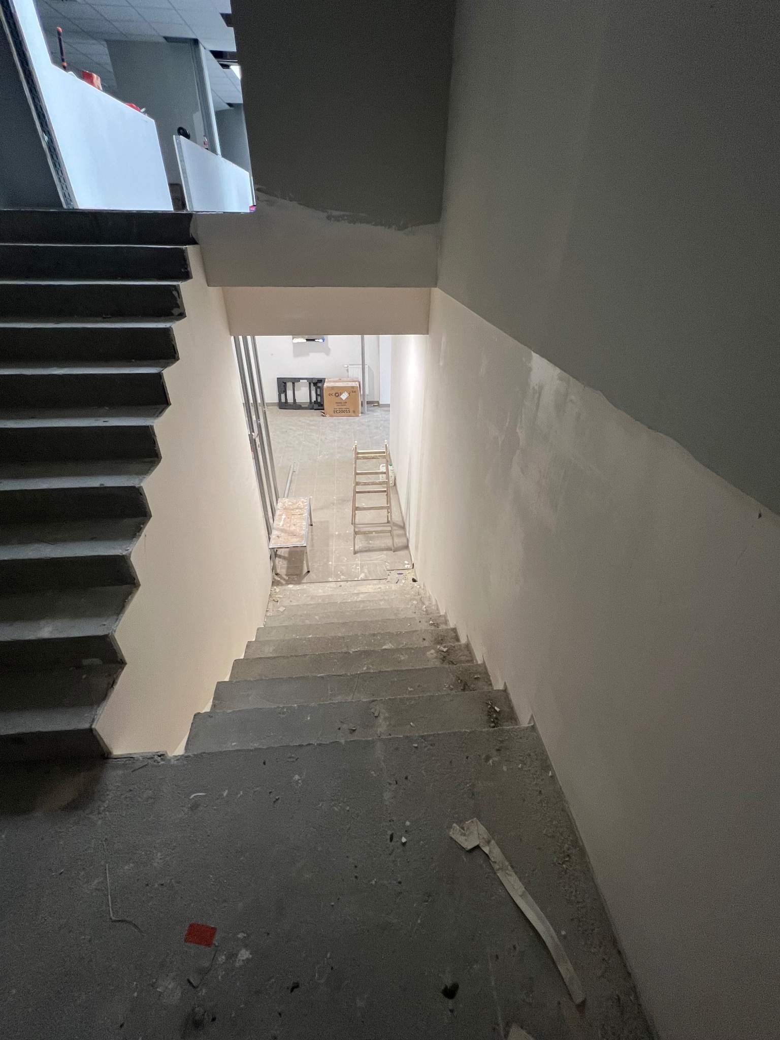 Klatka schodowa w surowym stanie, ściany przygotowane do malowania, widoczne ślady szpachlowania i drabina w tle.