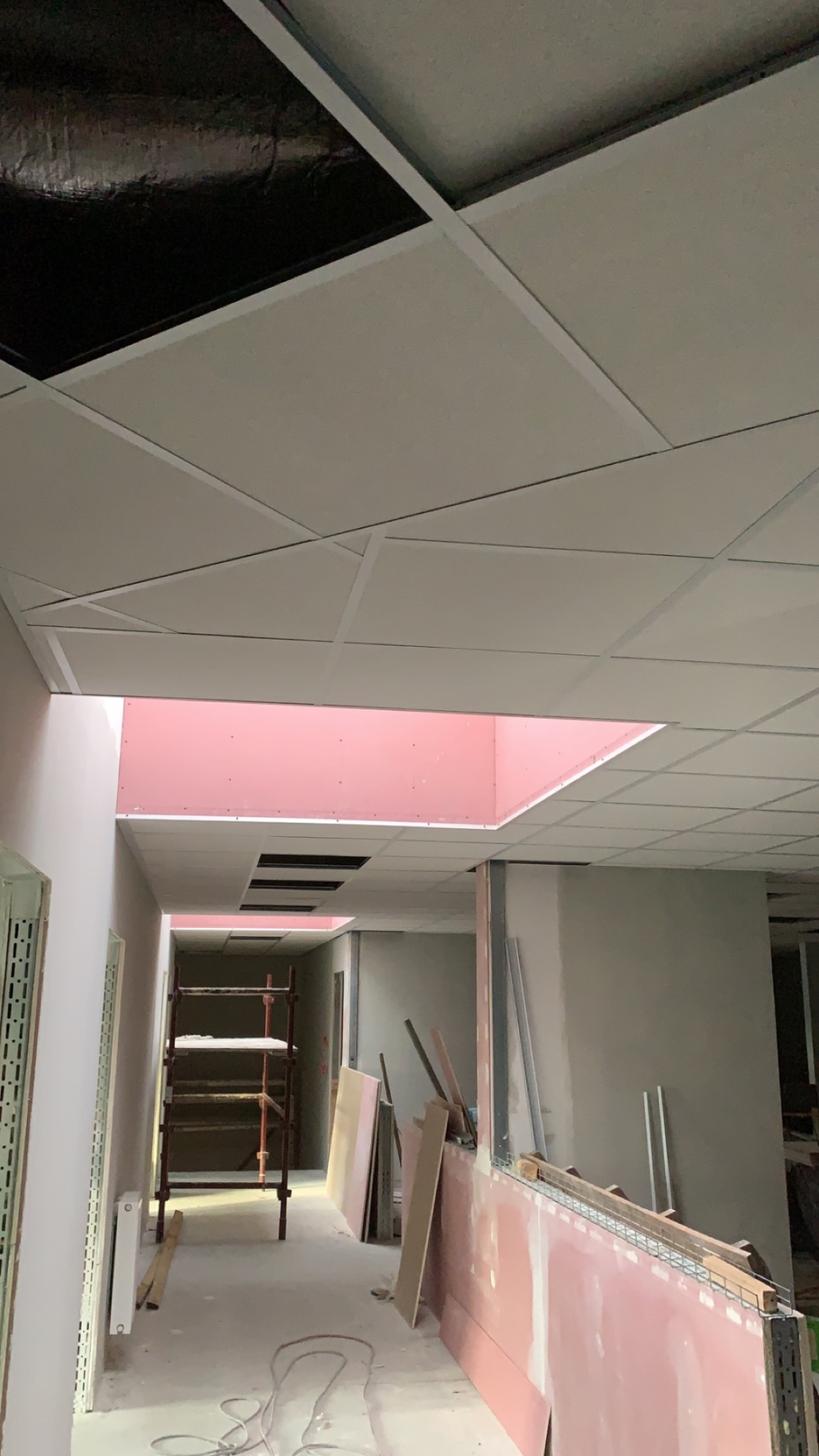 Montaż sufitu podwieszanego w biurze w Lesznie, widoczne płyty gipsowe i konstrukcja nośna, w tle fragmenty ścian z płyt gipsowo-kartonowych i rusztowanie.