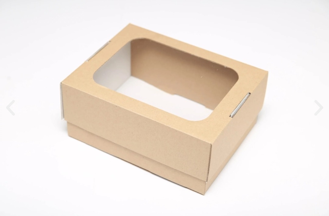 Puste, kwadratowe pudełko z brązowego kartonu z wyciętym okienkiem, widoczne zszywki na boku, na białym tle.