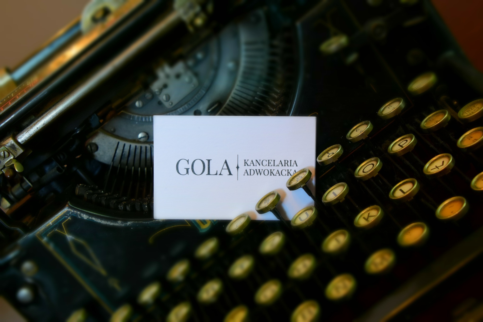Wizytówka Kancelarii Adwokackiej GOLA na tle starej maszyny do pisania z okrągłymi klawiszami.