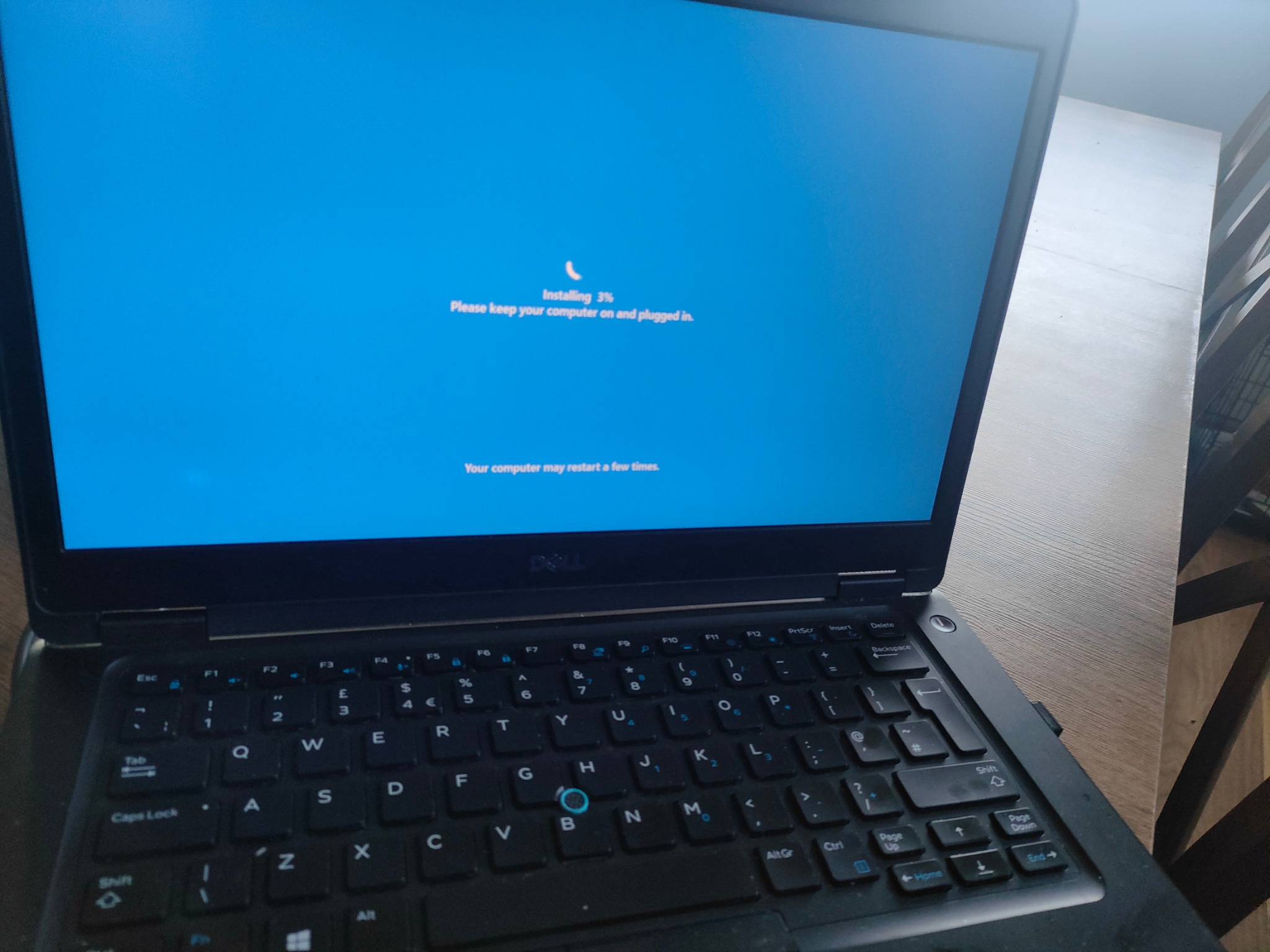 Laptop Dell z ekranem wyświetlającym proces instalacji, postęp 3%, z komunikatem o konieczności utrzymania zasilania i możliwości restartu.