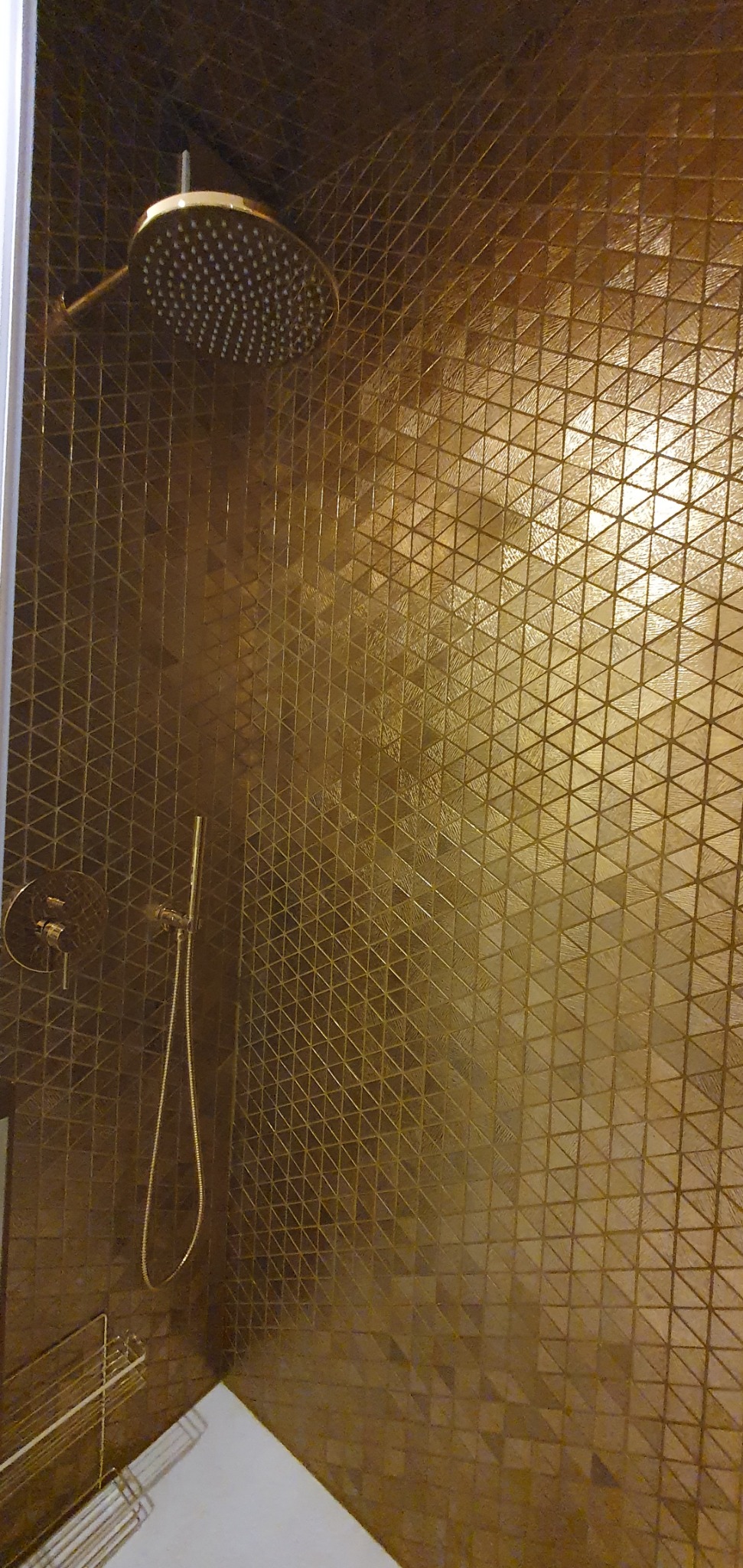 Kabina prysznicowa z deszczownicą i baterią w kolorze złotym, wykończona mozaiką z trójkątnych płytek w odcieniach brązu i złota.