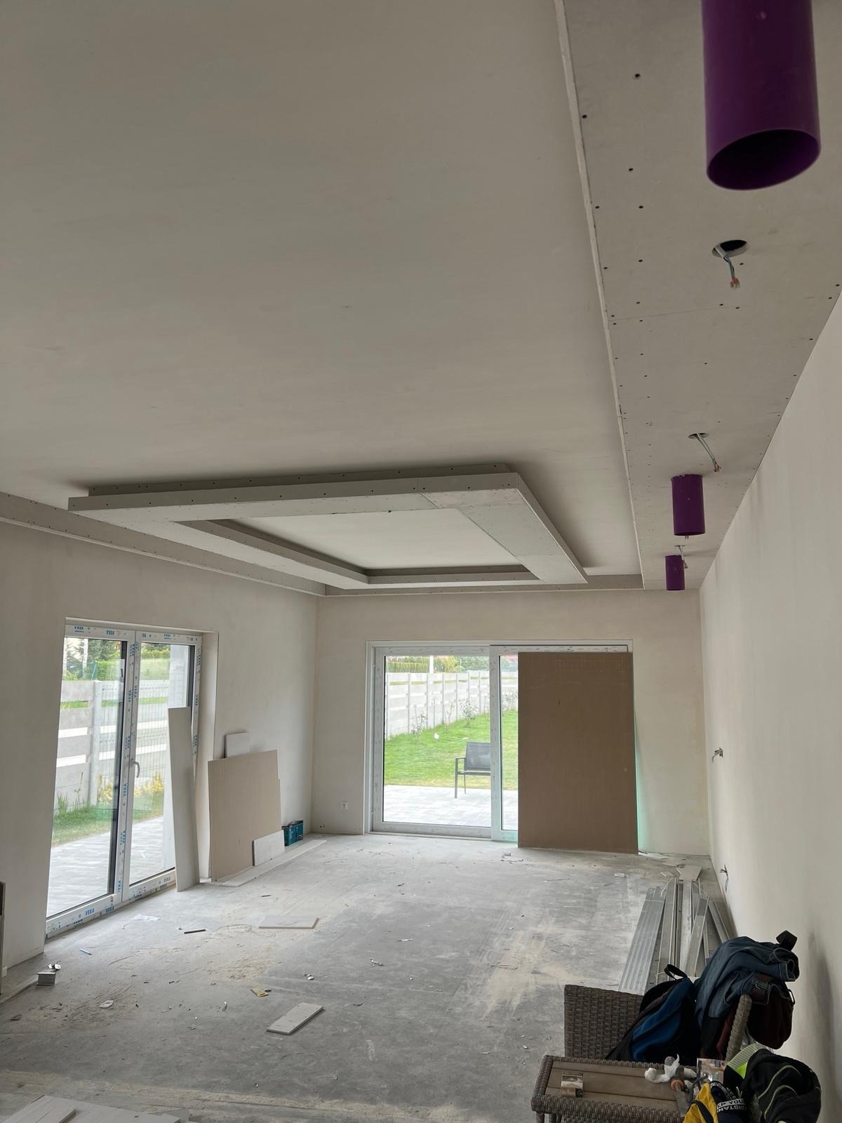 Surowy stan wnętrza z zamontowaną ramą sufitową z płyt karton-gips, widoczne ślady prac wykończeniowych i przygotowane otwory na oświetlenie.