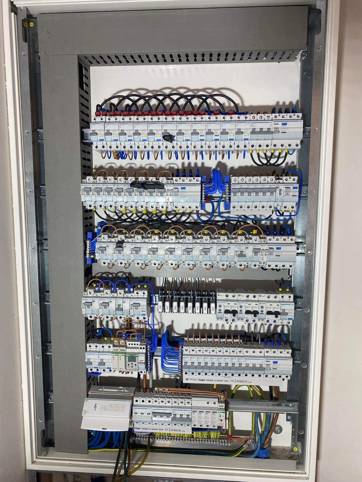 Rozdzielnia elektryczna z licznymi zabezpieczeniami nadprądowymi i różnicowoprądowymi, starannie połączona przewodami w kolorach czarnym, niebieskim, brązowym i żółto-zielonym, umieszczona...