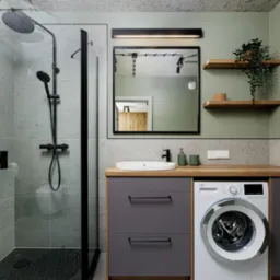 Nowoczesna łazienka z kabiną prysznicową typu walk-in, umywalką nablatową z czarną armaturą, pralką Beko w zabudowie oraz drewnianymi półkami z rośliną pnącą na pistacjowej ścianie.