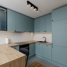 Wiktoria Rola - Nowoczesna kuchnia w odcieniach błękitu z drewnianymi blatami, czarnymi akcentami i wzorzystą podłogą w paski, oświetlona listwami LED pod szafkami górnymi.