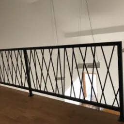 Nowoczesna balustrada wewnętrzna z czarnych, metalowych prętów tworzących geometryczny wzór krzyży, zamontowana na drewnianej podłodze, z widocznymi lampami wiszącymi i oknem w tle.