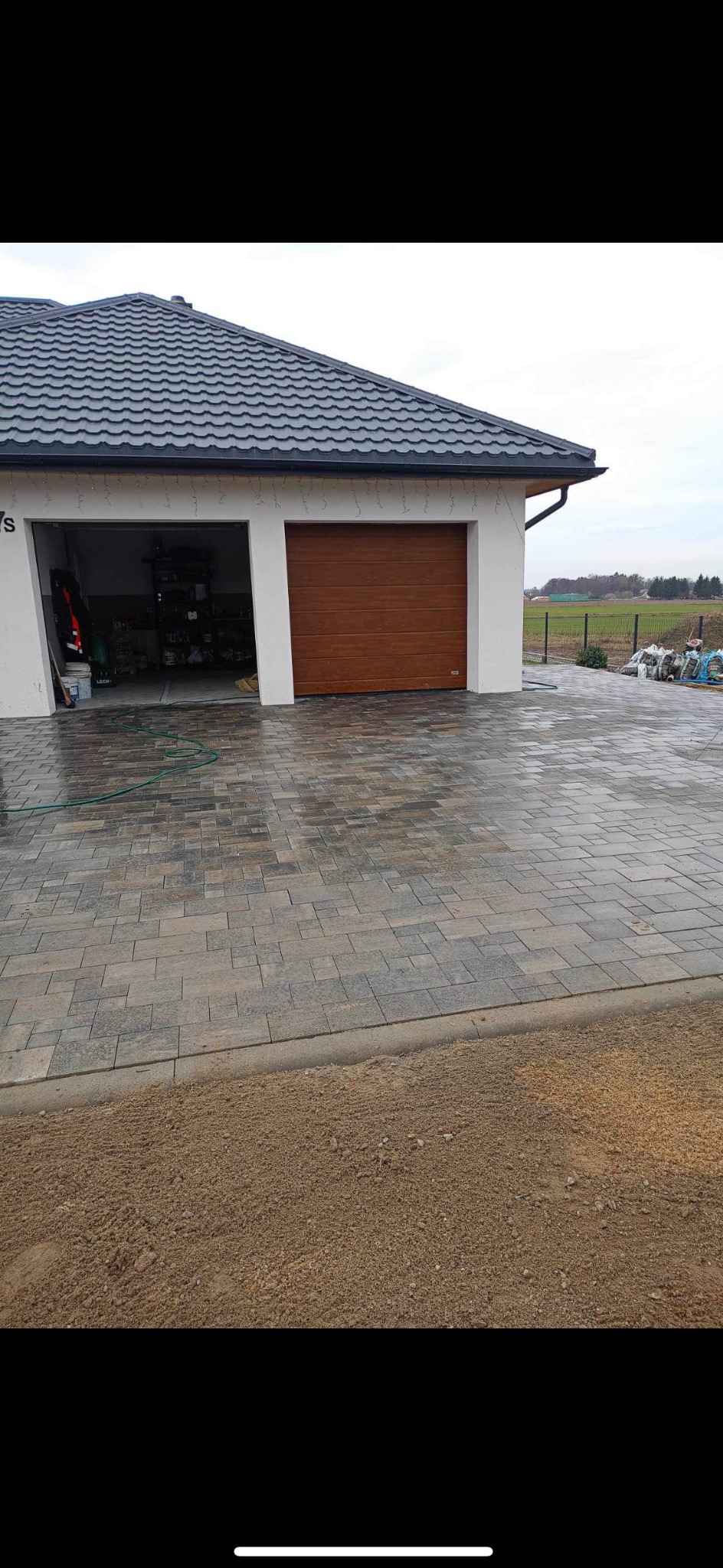 Ułożona kostka brukowa na podjeździe przed garażem, widoczny obrzeżnik i przygotowane podłoże z piasku.