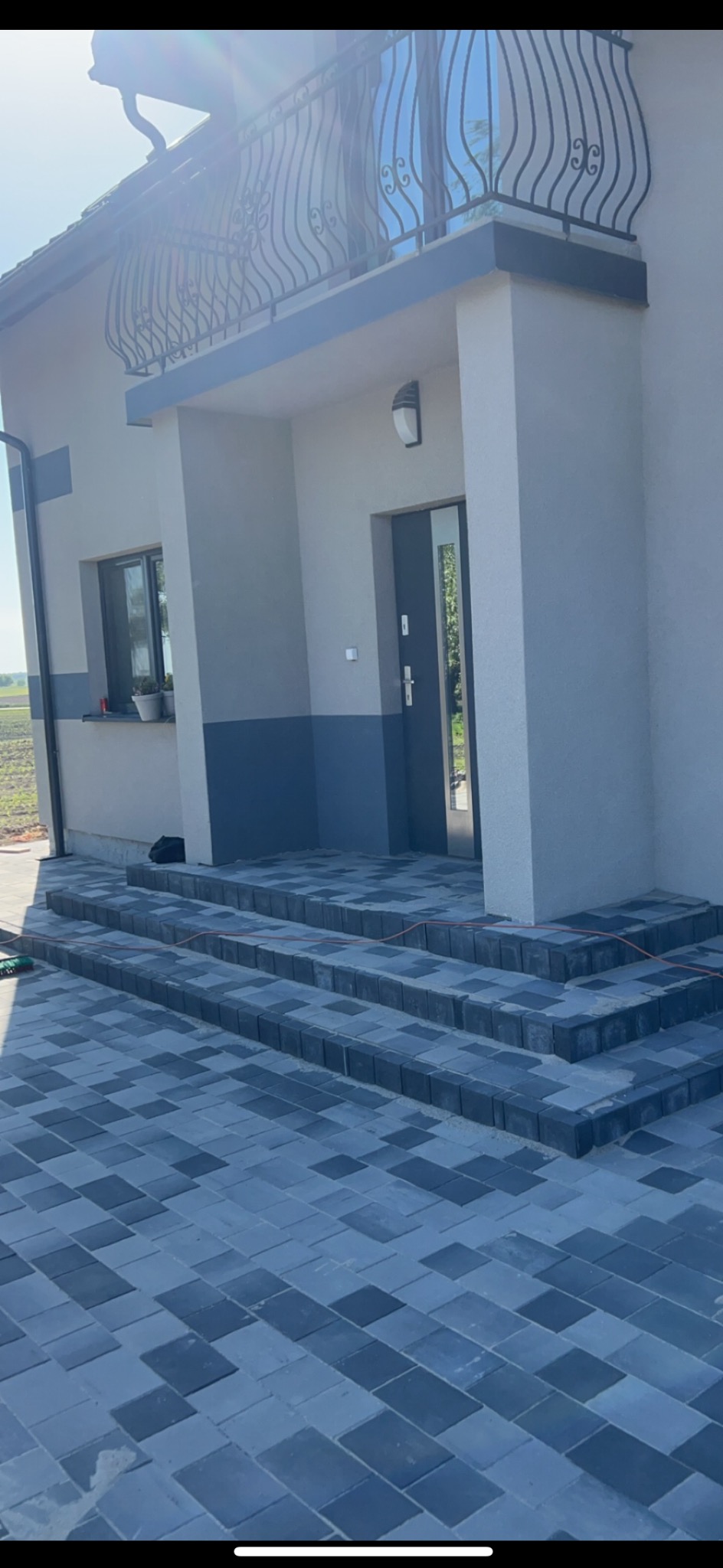 Nowoczesne schody wejściowe do domu wyłożone szaro-grafitową kostką brukową w diagonalny wzór, dopasowane kolorystycznie do elewacji budynku.