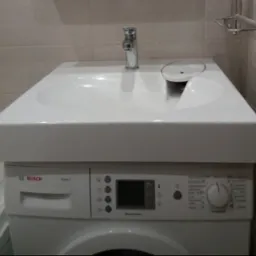 Biała umywalka nablatowa z chromowaną baterią zamontowana bezpośrednio na pralce Bosch Maxx 5 w łazience z jasnymi płytkami.