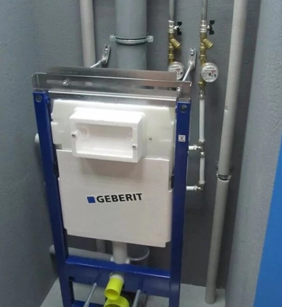 Stelaż podtynkowy Geberit zamontowany w surowym wnętrzu z widocznymi rurami i zaworami.