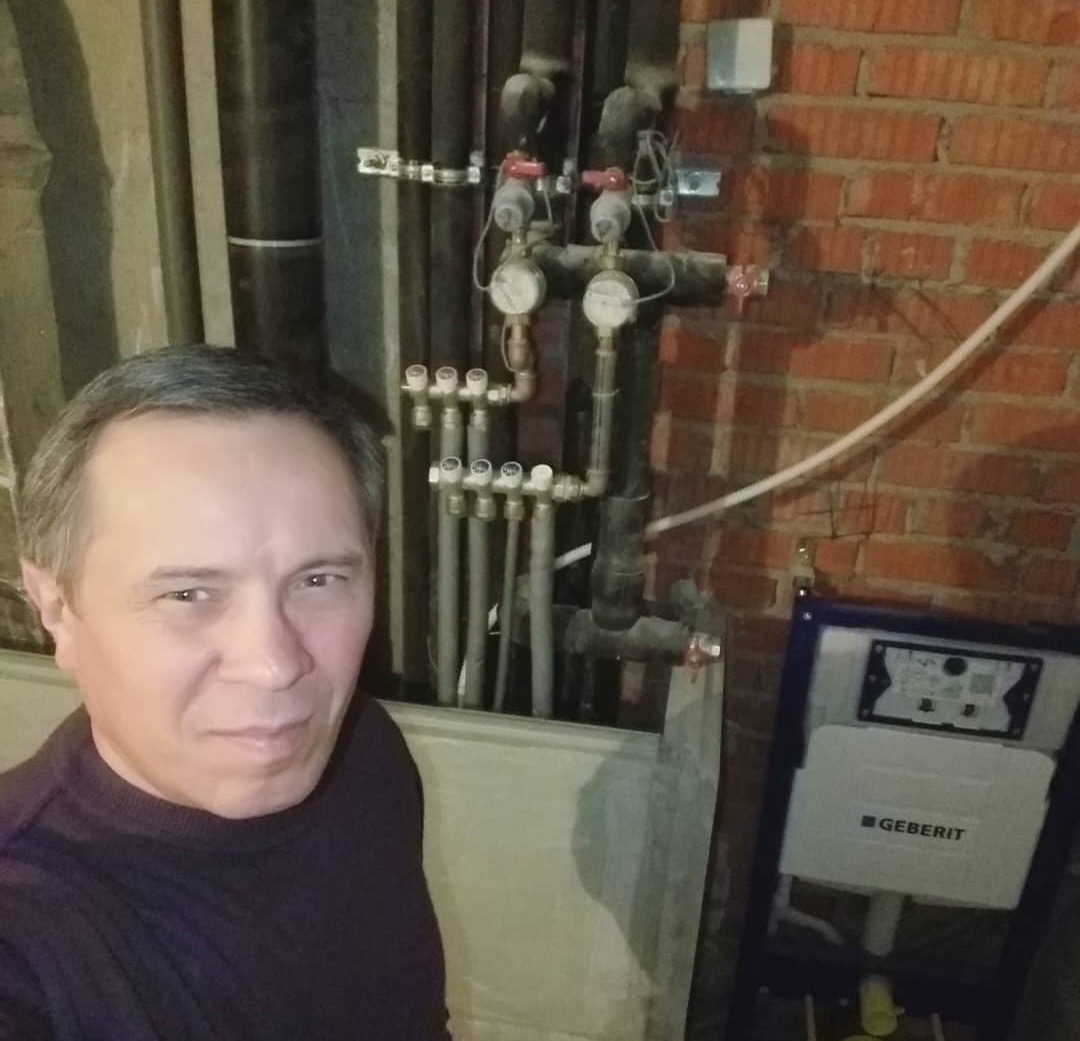 Instalacja wodna z rurami, zaworami, manometrami i stelażem podtynkowym Geberit na tle ściany z cegły, widok z perspektywy osoby fotografującej.