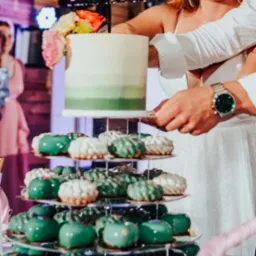 Nowożeńcy kroją tort weselny z zielonym ombre i piramidą zielonych i białych deserów na przezroczystym stojaku.