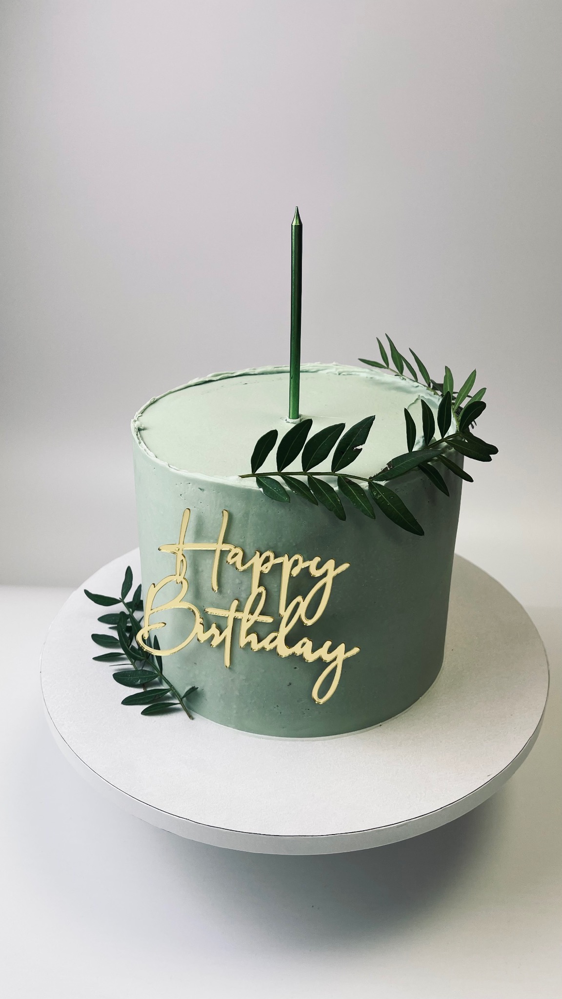 Tort w odcieniach zieleni z napisem 'Happy Birthday', świeczką i dekoracją z gałązek, wykonany w Bielawie.