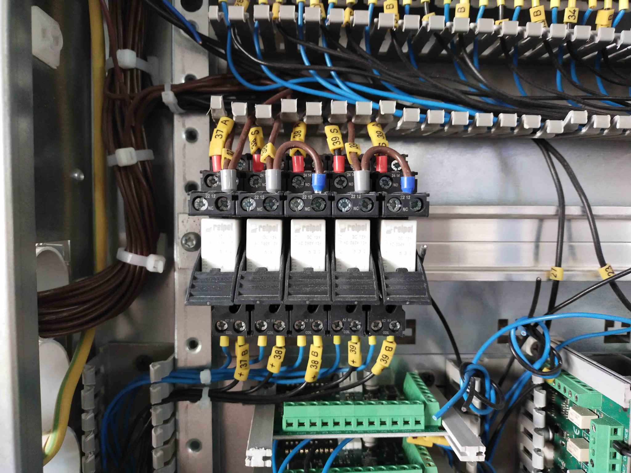 Wnętrze szafy sterowniczej z widocznymi przekaźnikami Relpol, okablowaniem oznaczonym numerami 37, 38, 39 oraz listwami zaciskowymi w kolorze zielonym i niebieskim.