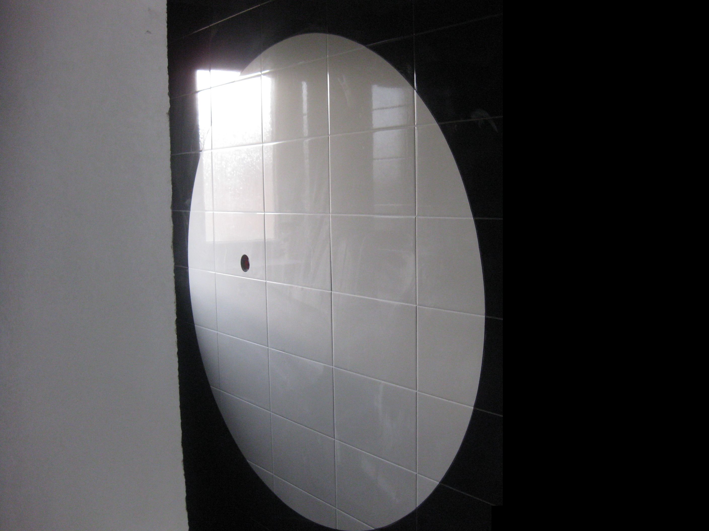 Ściana łazienki z czarno-białymi płytkami ułożonymi w okrągły wzór, widoczny otwór na rurę w białej części, ściana w trakcie prac wykończeniowych.