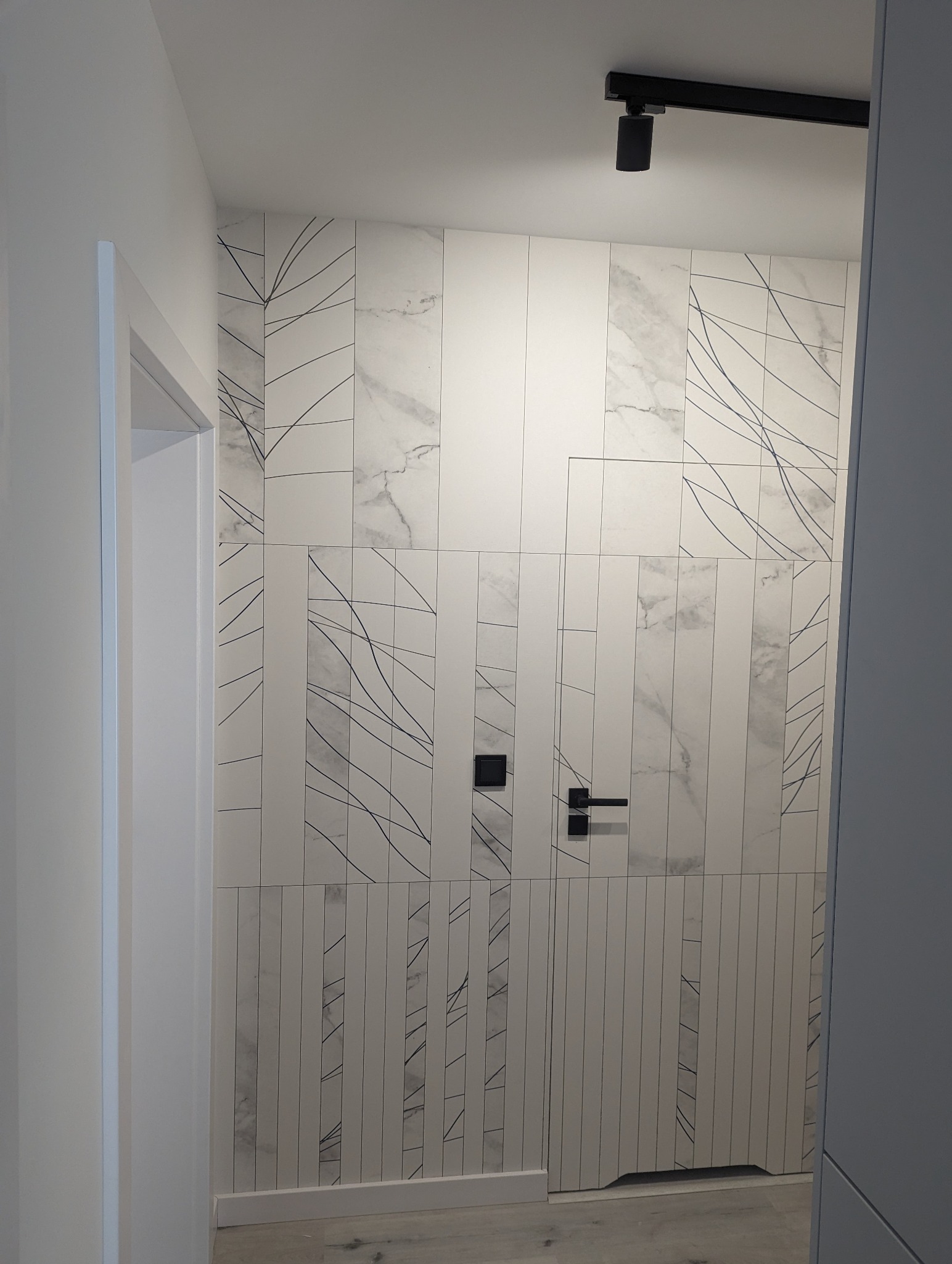 Nowoczesna łazienka z białymi płytkami imitującymi marmur, zdobionymi czarnymi liniami, czarna armatura i oświetlenie punktowe