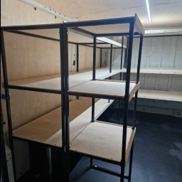 Jakub Wcisło - Metalowa konstrukcja regału z drewnianymi półkami, zamontowana wewnątrz furgonetki, widoczne mocowania do ściany pojazdu.