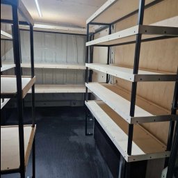 Jakub Wcisło - Metalowa konstrukcja regałów z drewnianymi półkami zamontowana wewnątrz furgonetki z oświetleniem LED na suficie, widoczne ślady użytkowania pojazdu.