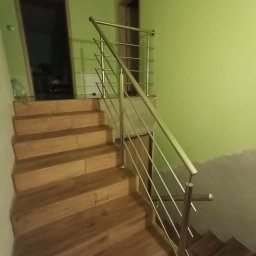 Jakub Wcisło - Schody wewnętrzne z drewnianymi stopniami i prostą, nowoczesną balustradą ze stali nierdzewnej, widok z dołu, ściana pomalowana na zielono.