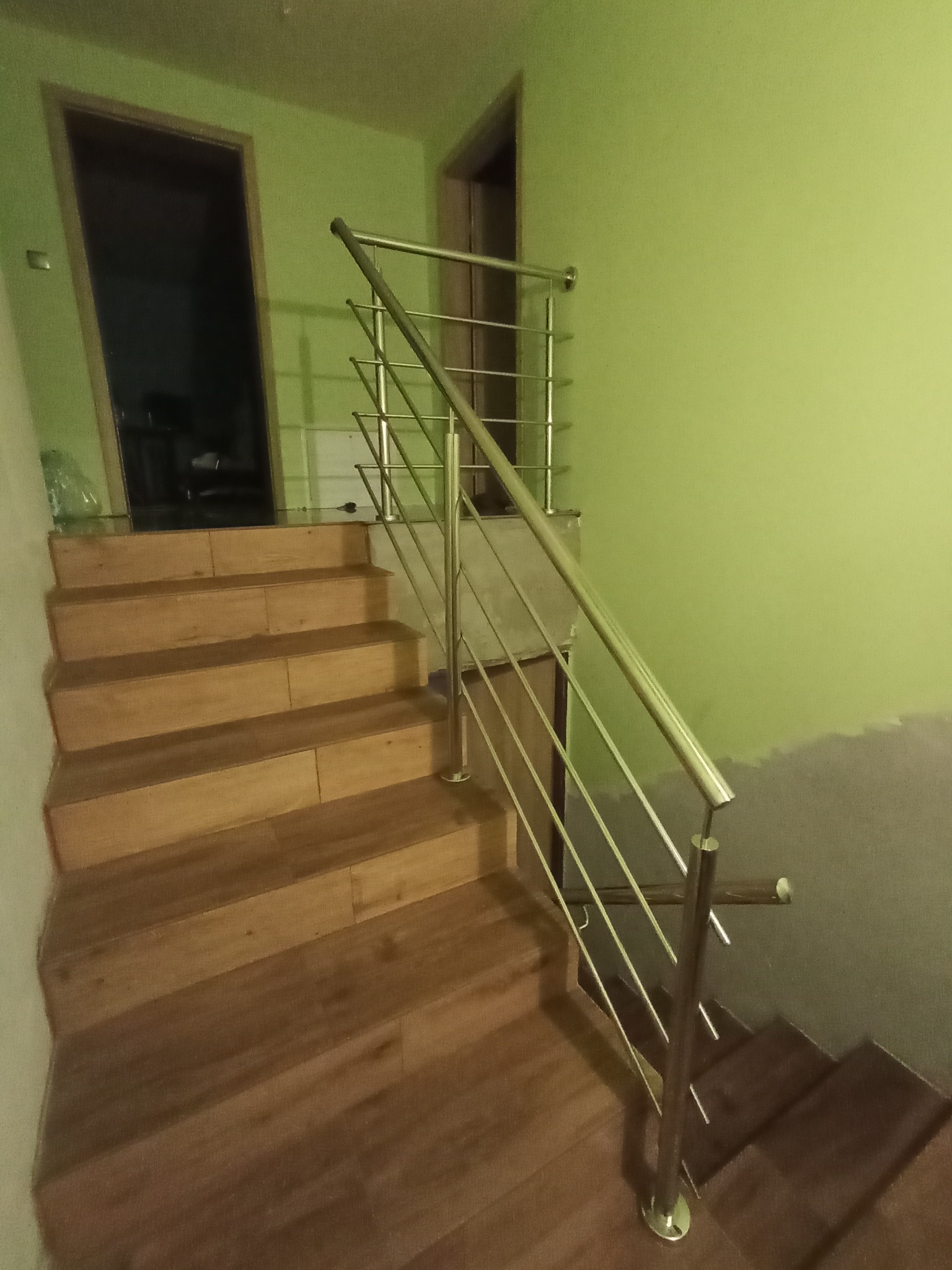 Schody wewnętrzne z drewnianymi stopniami i prostą, nowoczesną balustradą ze stali nierdzewnej, widok z dołu, ściana pomalowana na zielono.
