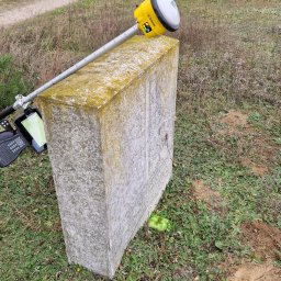 Usługi Geodezyjne Azymut - Tomasz Naworyta - Żółty odbiornik GNSS Trimble na betonowym słupku geodezyjnym, w tle polna droga i drzewa. Widoczny kontroler polowy.