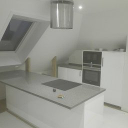 Budowar - Kuchnia z szarą wyspą i oknem dachowym w Morągu, w trakcie prac wykończeniowych, widoczne zabezpieczenia podłogi taśmą malarską.