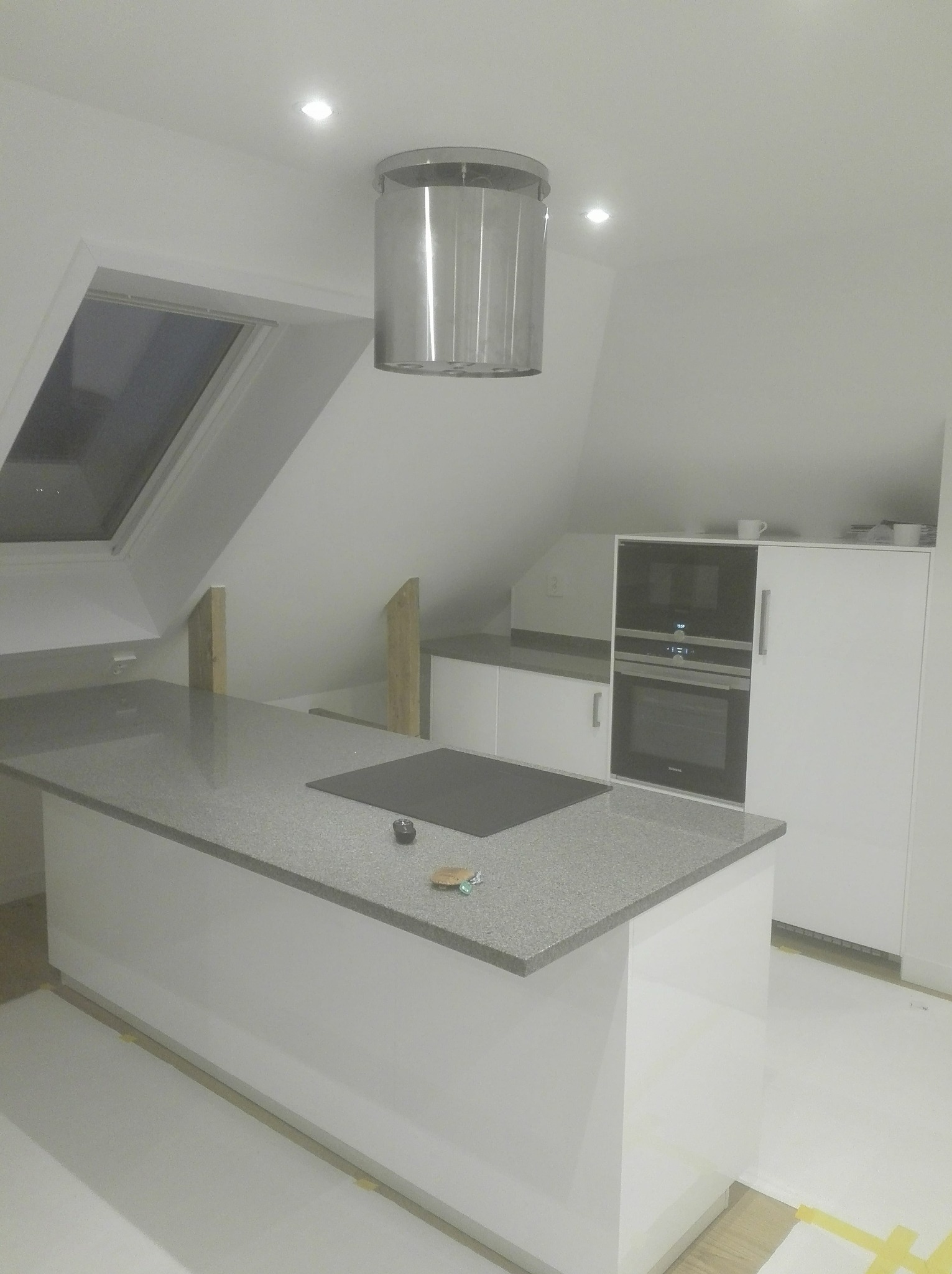 Kuchnia z szarą wyspą i oknem dachowym w Morągu, w trakcie prac wykończeniowych, widoczne zabezpieczenia podłogi taśmą malarską.