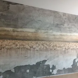 Ściana w Gdańsku z fototapetą przedstawiającą stado flamingów na tle pochmurnego nieba, imitująca efekt starego, popękanego tynku.