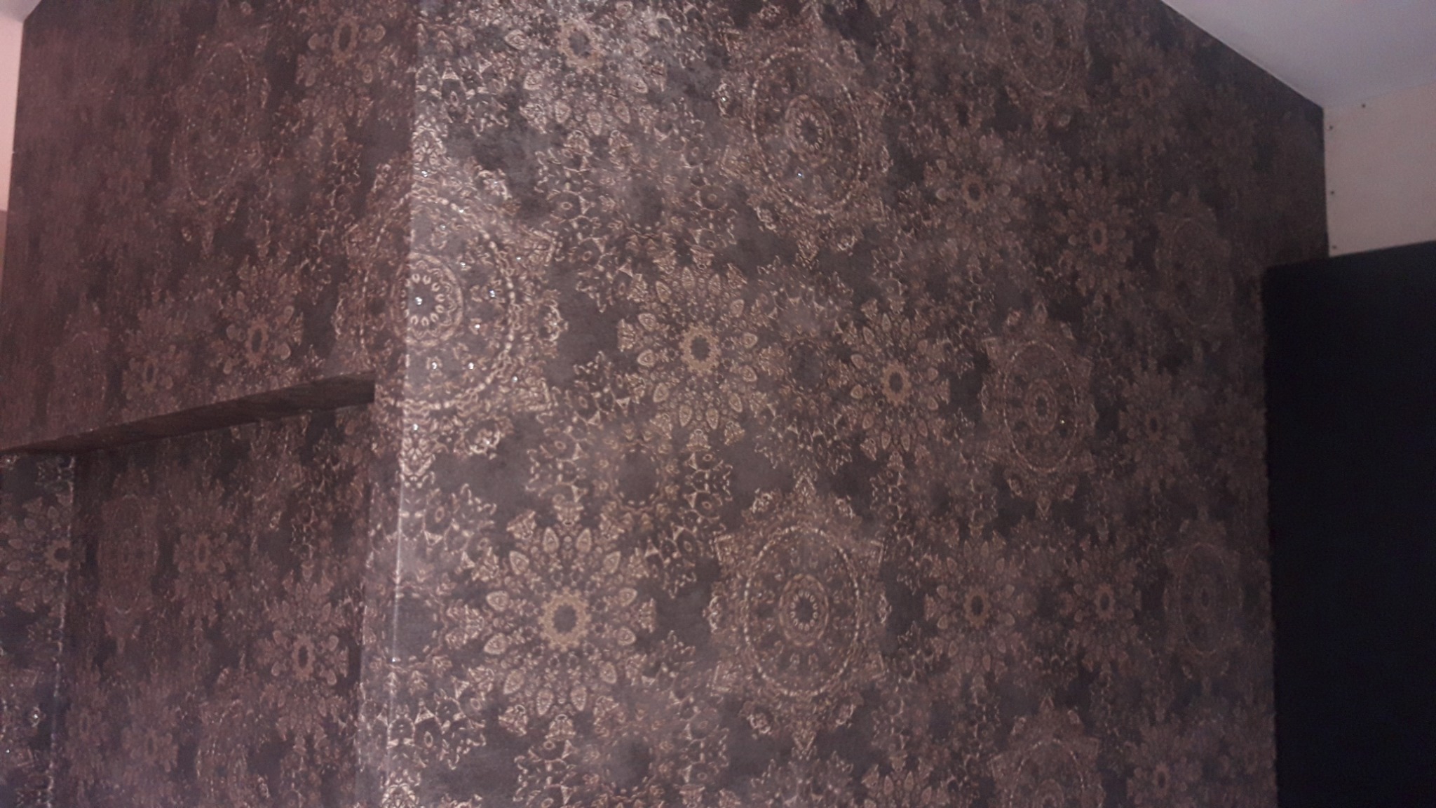 Wnętrze z ciemną, wzorzystą okładziną ścienną w stylu vintage, z motywem kwiatowym i geometrycznym, tworzącym unikalną fakturę na ścianach i wnęce.