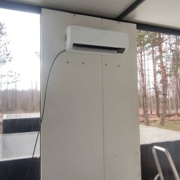 Duo Termika Paweł Tarkowski - Zamontowany klimatyzator SAMSUNG na białej ścianie w pomieszczeniu z widokiem na drzewa i drabinką.