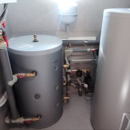 Duo Termika Paweł Tarkowski - Dwa szare zbiorniki akumulacyjne Ferroli w kotłowni z szarymi płytkami, widoczne rury miedziane, zawory i instalacja hydrauliczna, zasilanie elektryczne poprowadzone w peszlu.